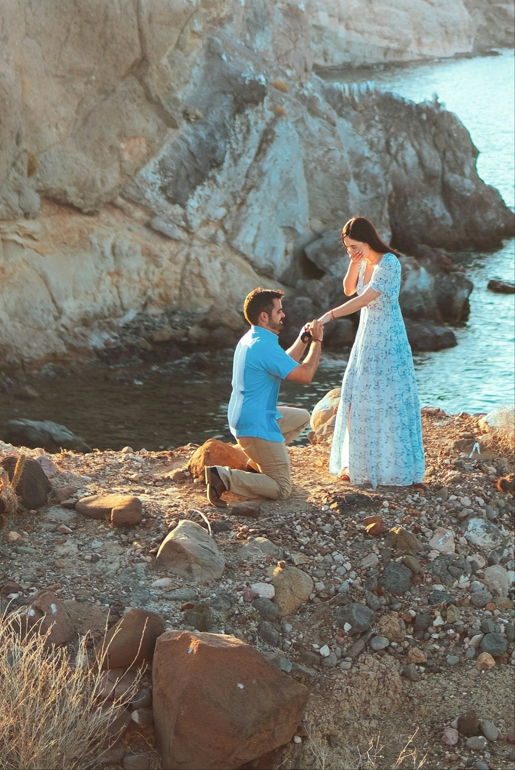 Two people standing on a rocky cliff overlooking the ocean.